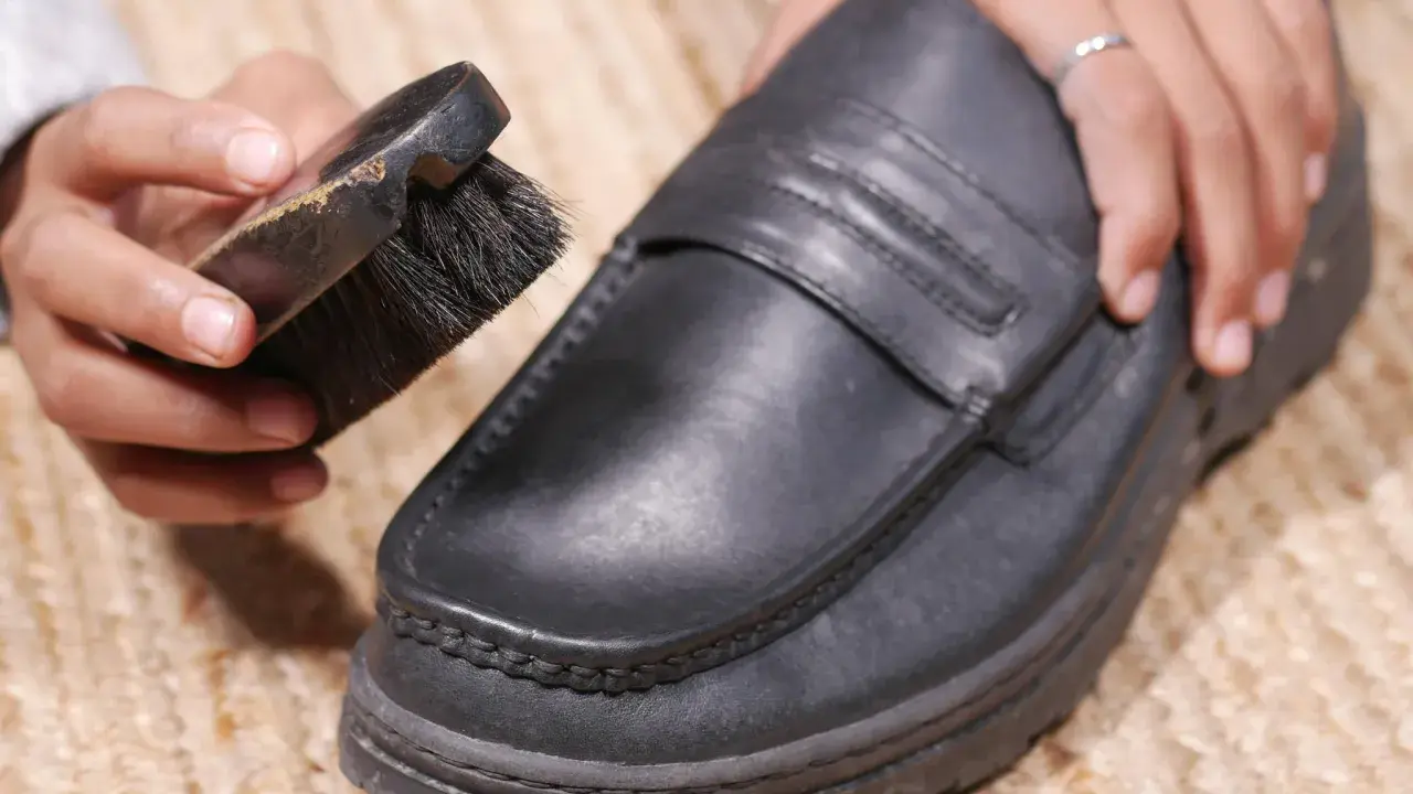 Hände reinigen einen schwarzen Lederschuh mit einer Bürste.