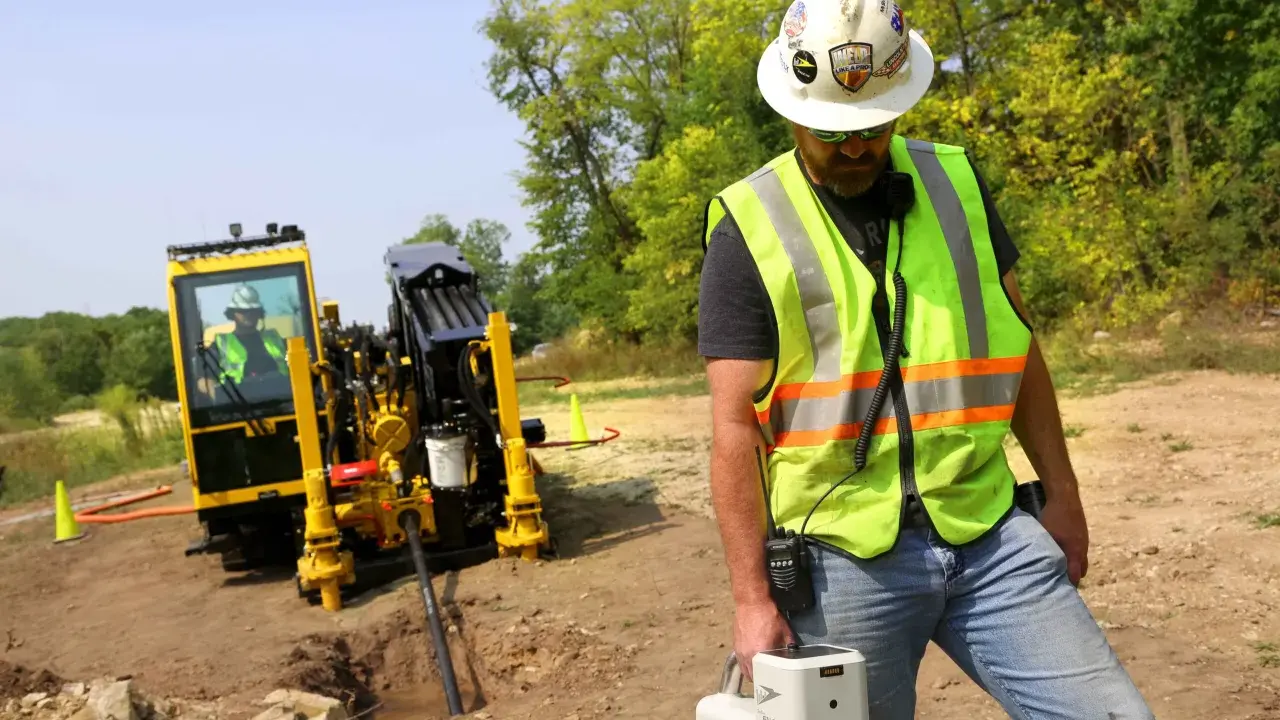 Trabajador supervisa una perforación horizontal dirigida con equipo especializado en un sitio de construcción.