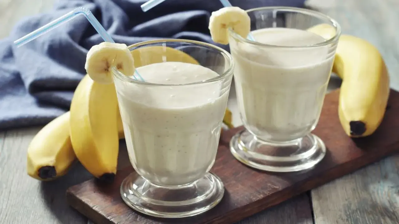 Dwa bananowe koktajle proteinowe w szklankach z rurkami i plasterkami banana. Idealne, gdy pić shake proteinowy po treningu.