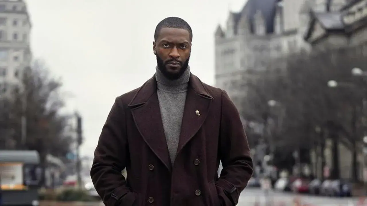 Alex Cross, un uomo con un cappotto scuro e un dolcevita grigio, guarda intensamente verso l'obiettivo.