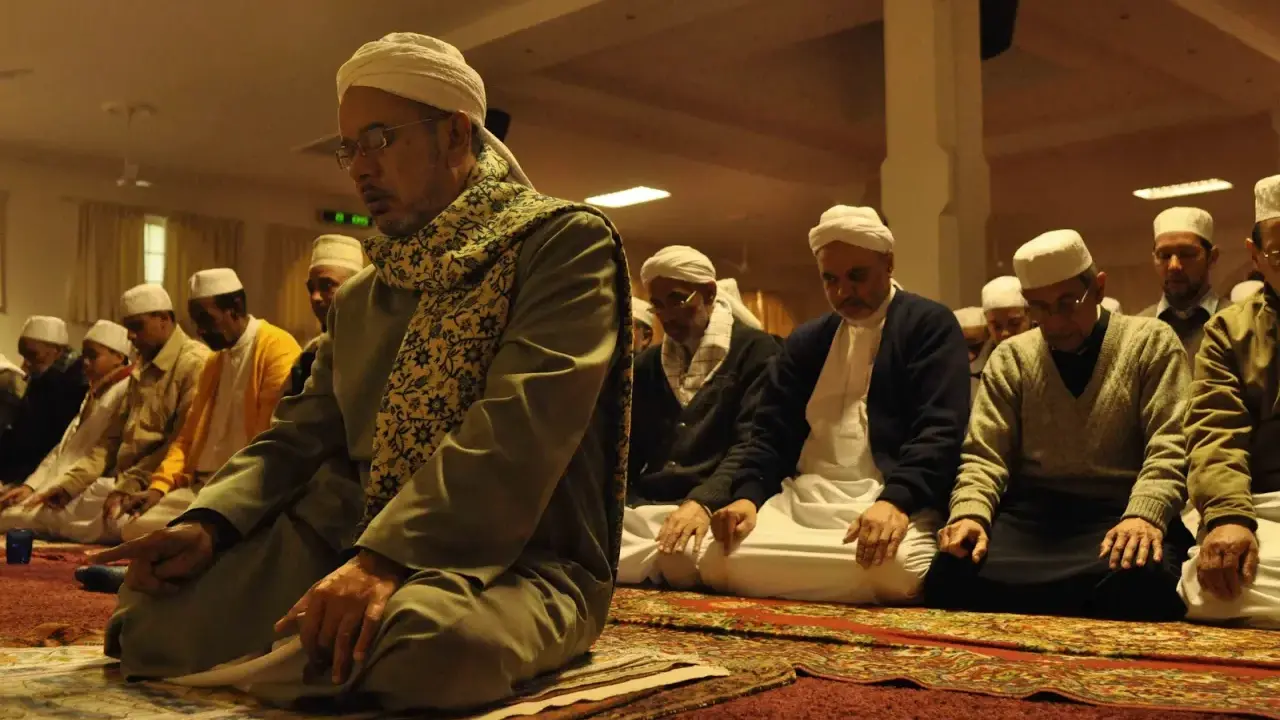 Männer in weißen Turbanten und traditioneller Kleidung knien auf Gebetsteppichen und verrichten das Taraweeh-Gebet.