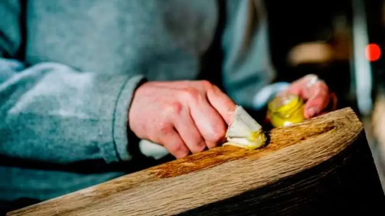 Manos aplicando cera a un trozo de madera, restaurando su brillo. El proceso de decapar madera revela su belleza natural.