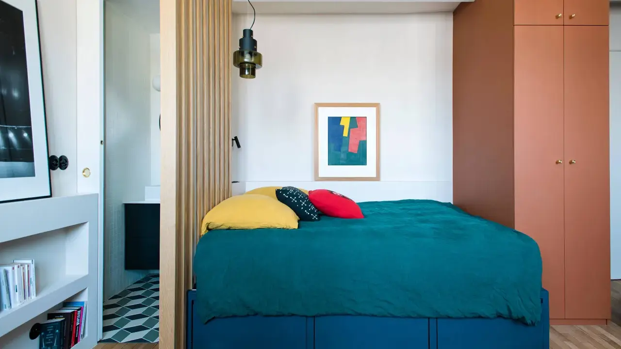 Une chambre cabine cosy avec un lit bleu canard, des coussins colorés et une armoire ocre. Un paravent en bois sépare l'espace nuit de la salle de bain.