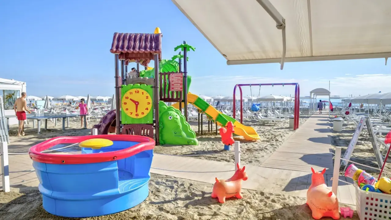 Area giochi su sabbia con scivolo, altalena e giochi d'acqua, un vero lido per bambini.