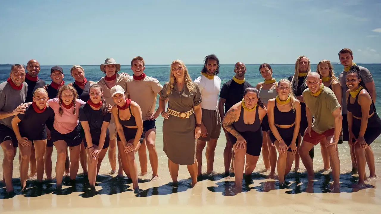 En grupp glada robinson deltagare poserar på en strand med havet i bakgrunden.
