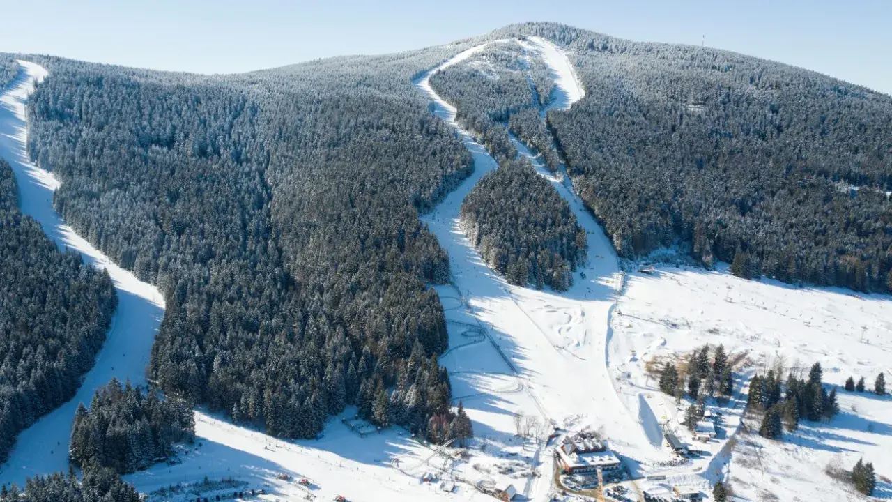 Widok z lotu ptaka na czarna góra resort, ośrodek górski z trasami narciarskimi wśród ośnieżonych lasów i budynkami u podnóża góry.