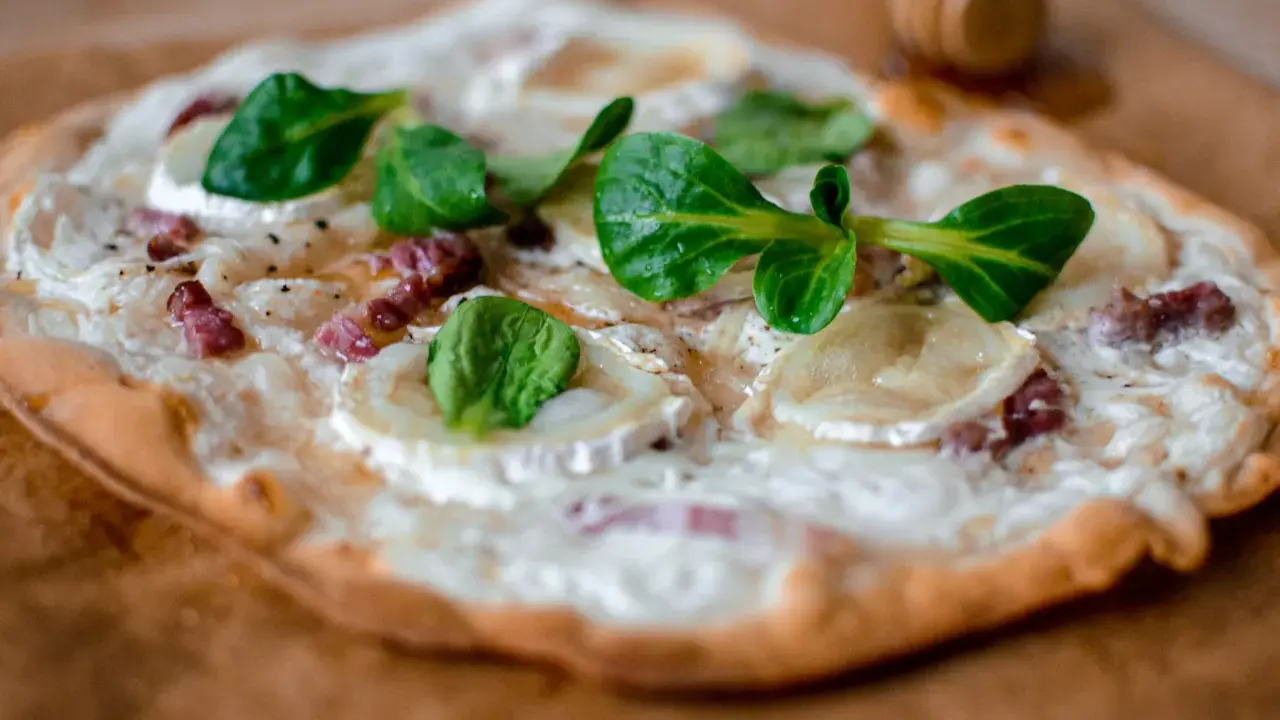 Tarte flambée alsacienne garnie de lardons, fromage de chèvre et jeunes pousses.