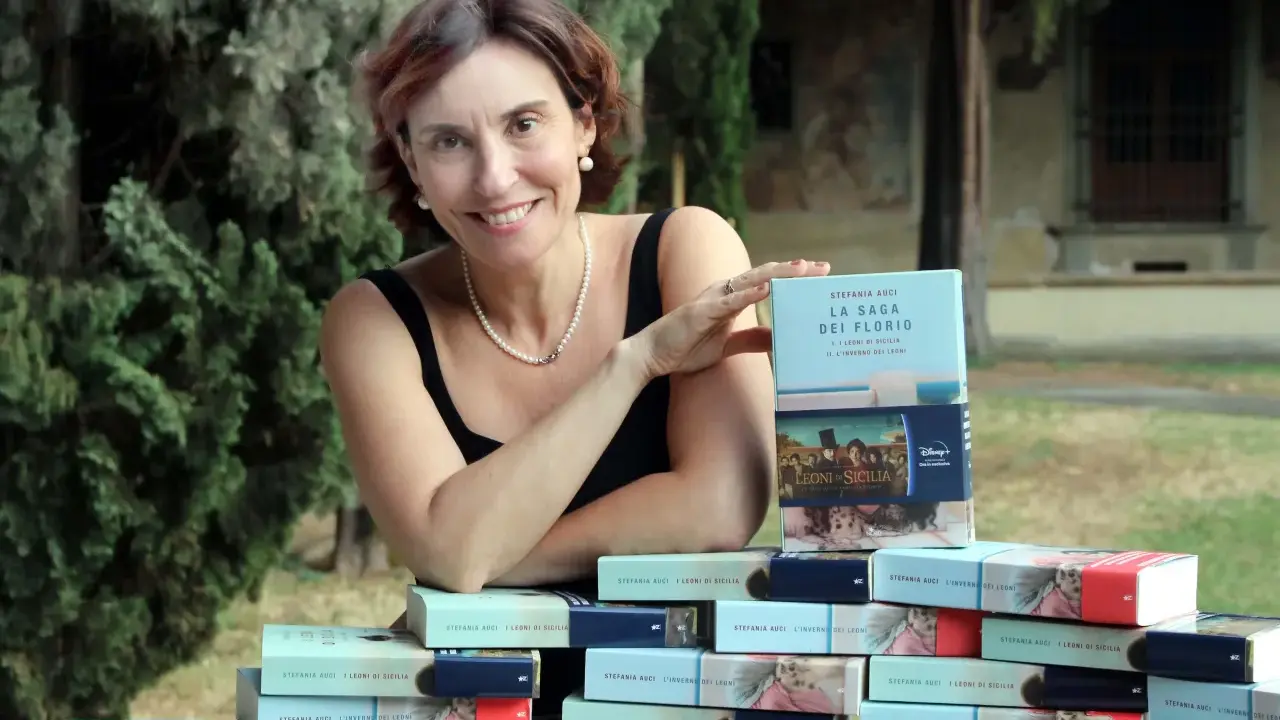 Stefania Auci sorride, circondata dai suoi libri "I Leoni di Sicilia" e "L'inverno dei leoni", celebrando il successo della saga.