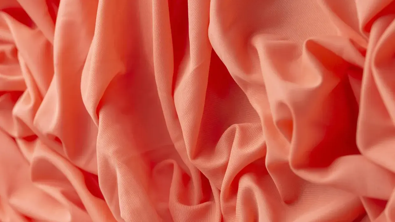 Tessuto arancione con pieghe morbide. Il materiale acrilico, cos'è? Una fibra sintetica versatile e resistente, ideale per abbigliamento e tessuti d'arredo.