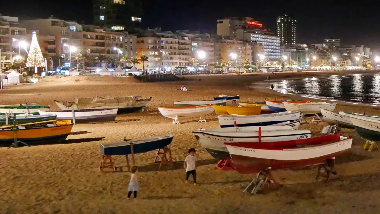 Boote am Strand bei Nacht, beleuchtete Stadt und Weihnachtsbaum. Selbst im Spanien Winter ist die Temperatur angenehm für einen Spaziergang.
