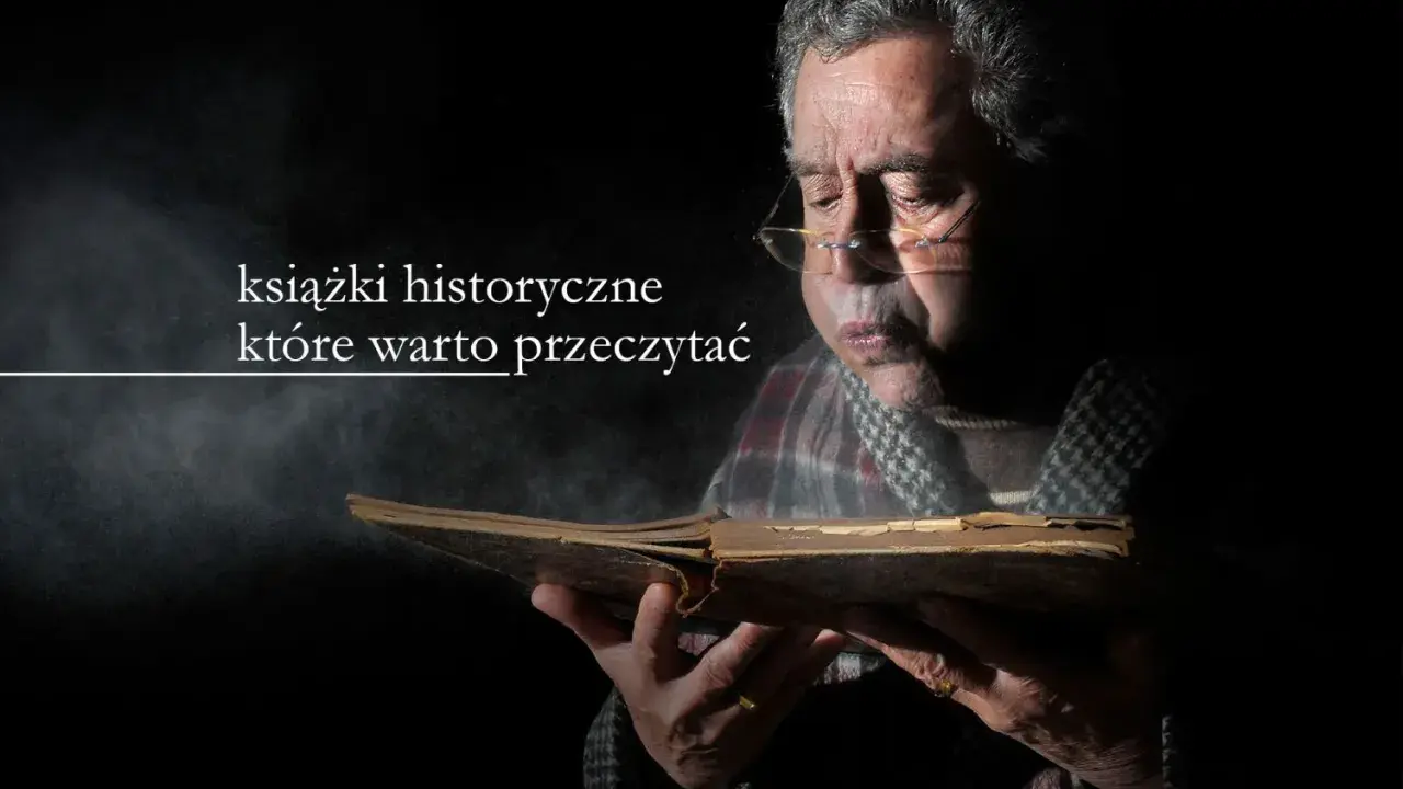 Starszy mężczyzna w okularach pochyla się nad starą księgą, zanurzając się w lekturze. Wokół unosi się pył, podkreślając atmosferę tajemnicy i wiedzy zawartej w książkach historycznych.
