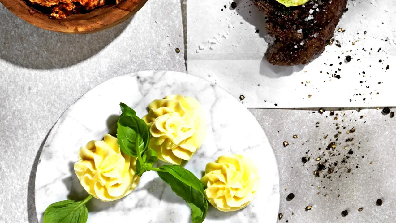 Ein Steak mit Kräuterbutter, dazu Kartoffelröschen und eine Schüssel mit einer roten Paste. Perfekt für ein knoblauchbutter rezept.