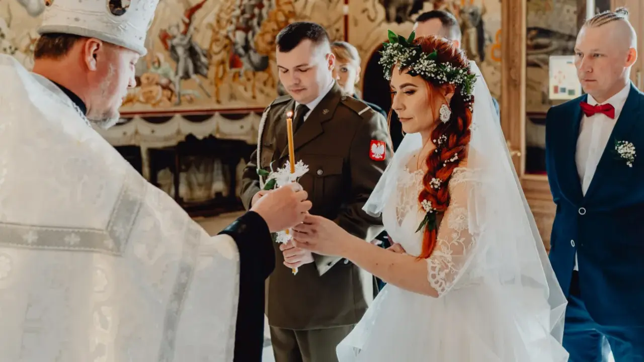 Uroczysty ślub prawosławny. Panna młoda w wianku, pan młody w mundurze, kapłan zapala świece.