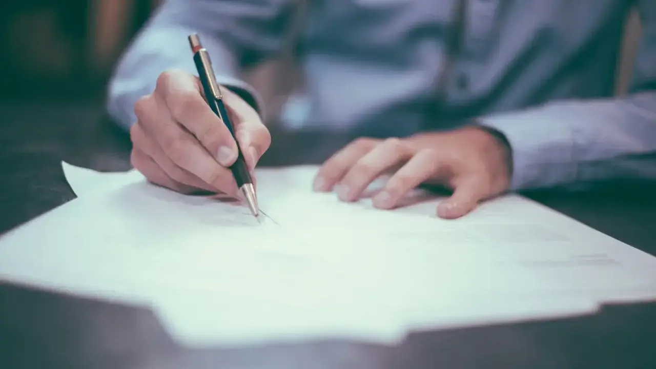 Dłoń pisze piórem na papierze, przygotowując list formalny angielski matura.