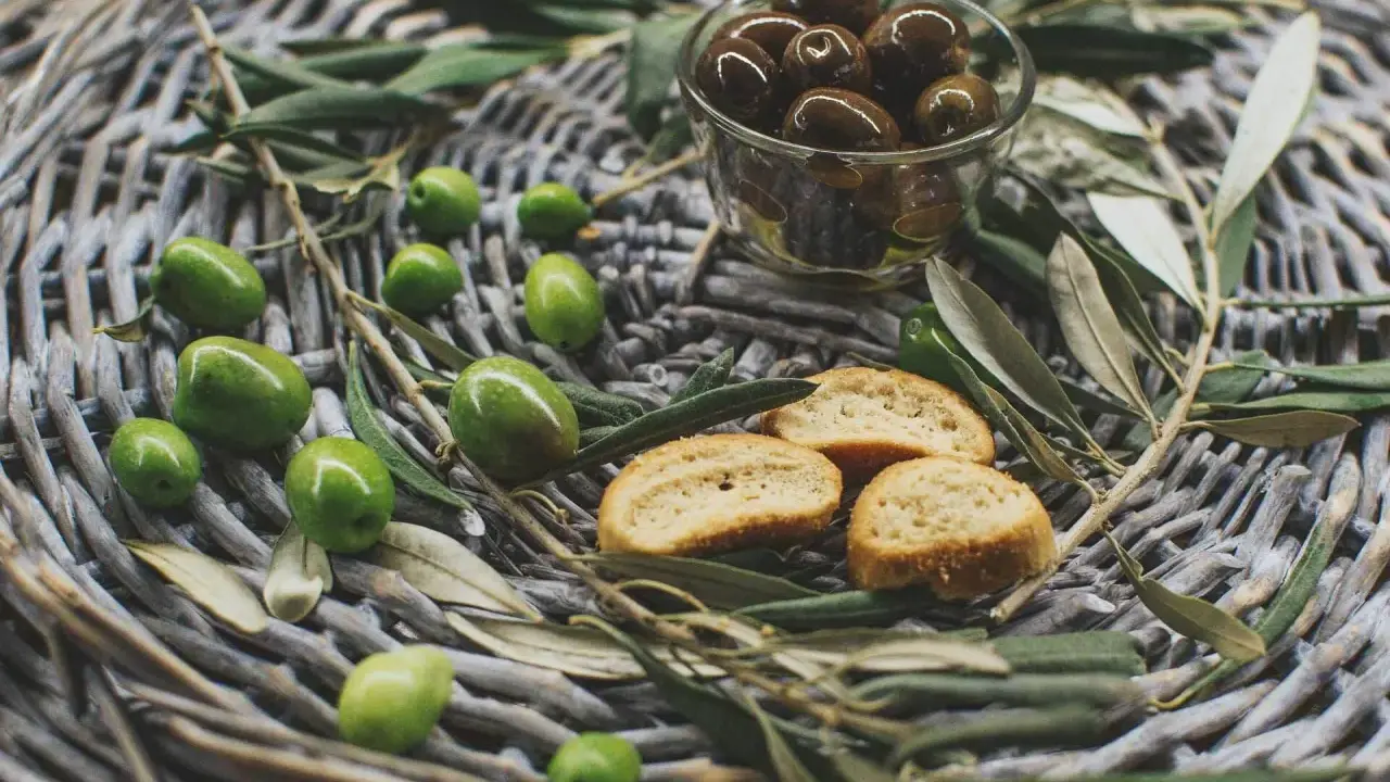 Olives vertes et noires, crostinis et feuilles d'olivier sur un panier tressé, évoquant une spécialité culinaire du Luberon.