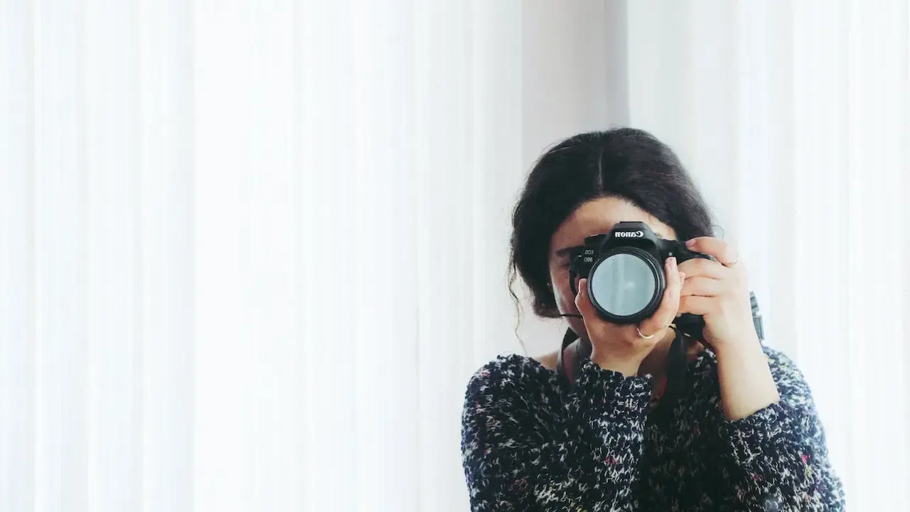 Kobieta z aparatem Canon, skupiona na kadrze. Rozwija swój biznes fotograficzny, łapiąc chwile.