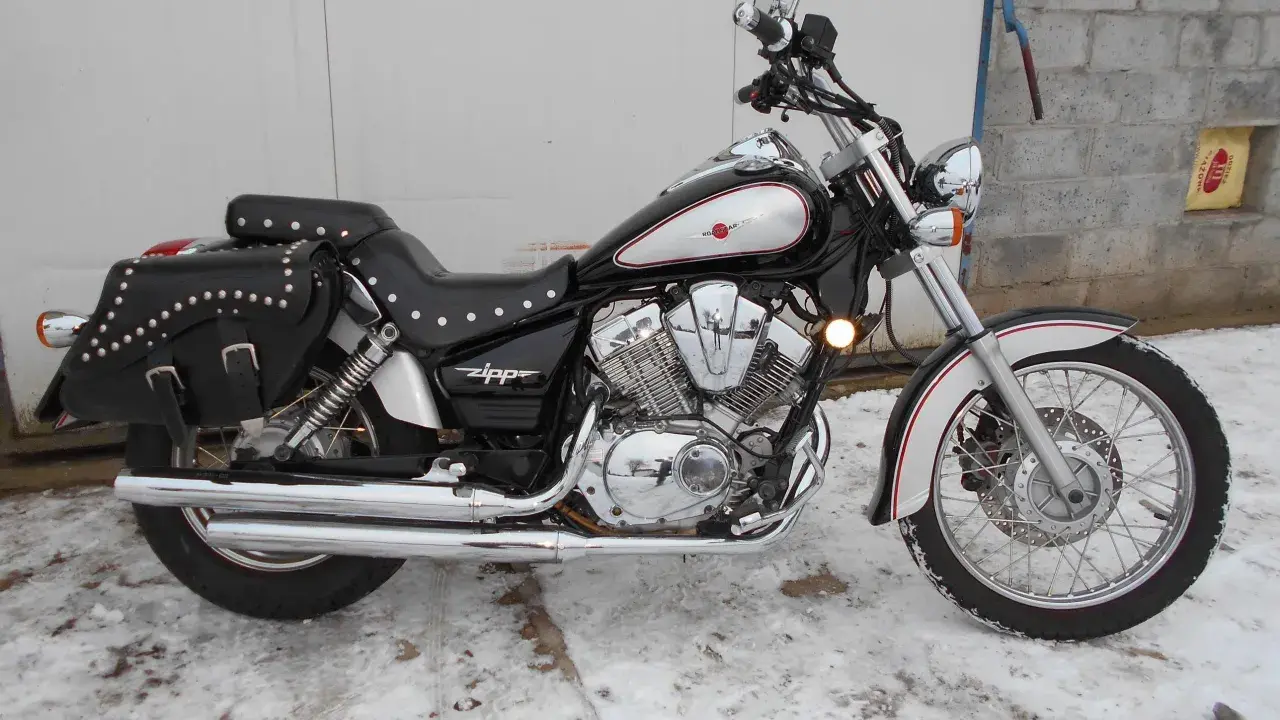 Czarny motocykl Zipp Roadstar 250 z sakwami, błyszczącymi chromami i ozdobnymi nitami, stoi na zaśnieżonym podjeździe.