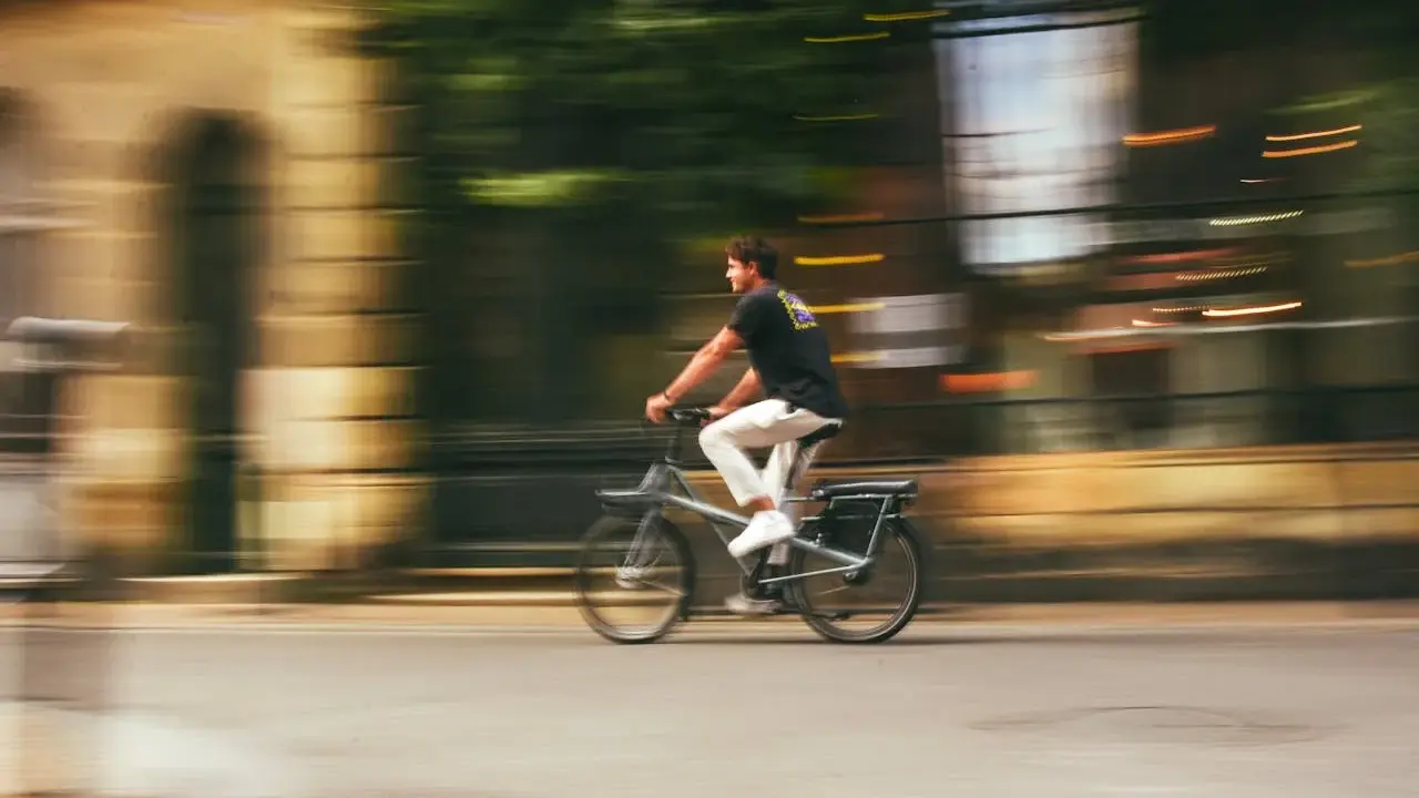 Mężczyzna na rowerze typu s-pedelec pędzi ulicą, rozmyte tło sugeruje dużą prędkość.