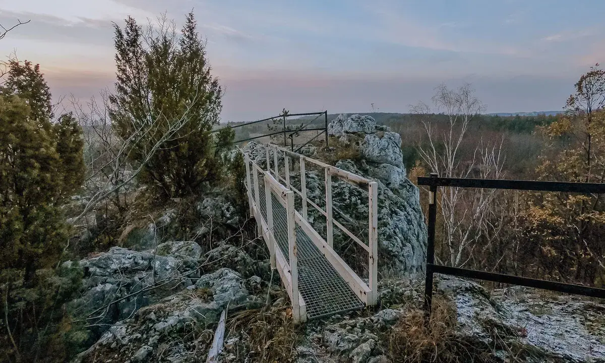 Mostek na skalnym ostańcu na Jurze Krakowskiej. W oddali las i niebo o zmierzchu.