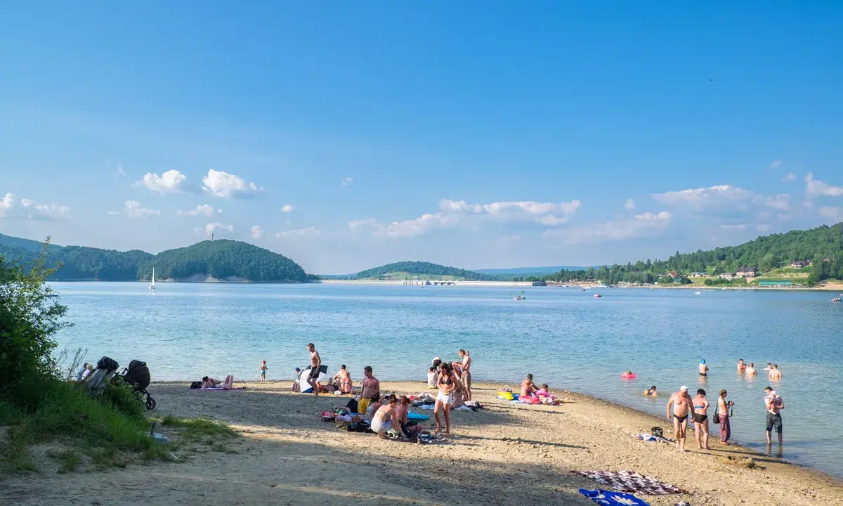 Polańczyk atrakcje: plażowicze odpoczywają nad Soliną, w tle żaglówka i zielone wzgórza.