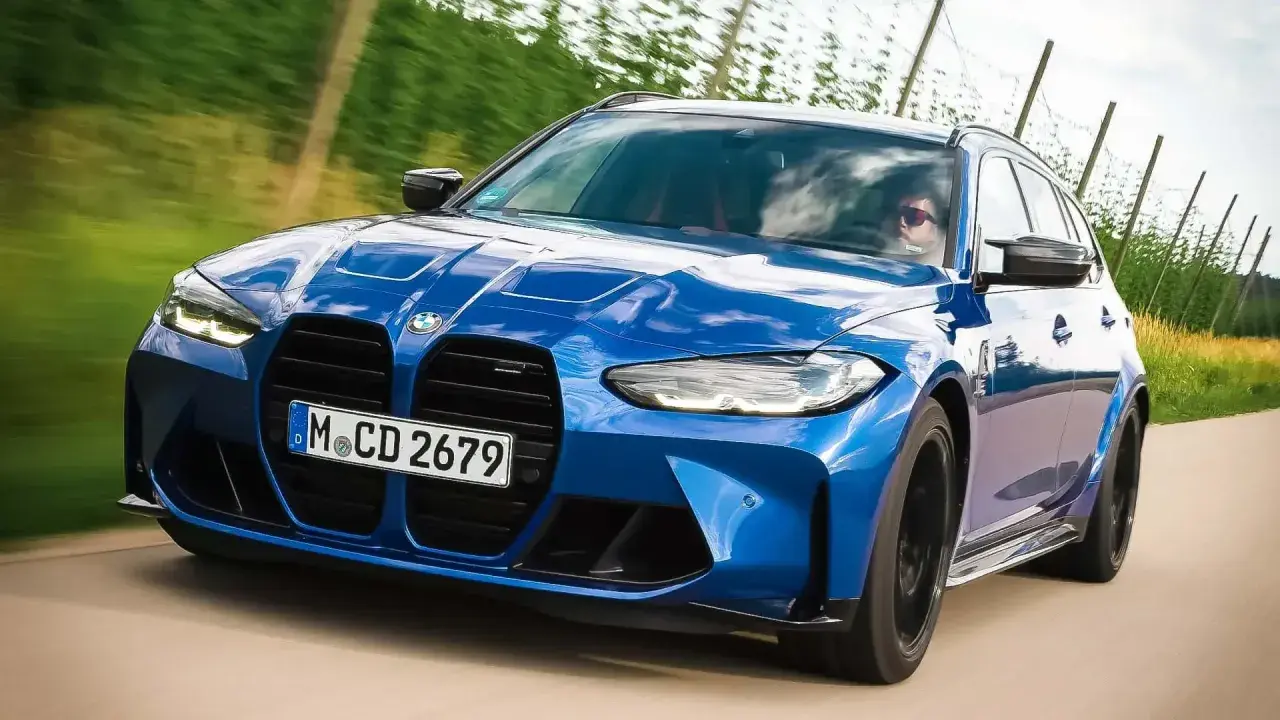 Blauer BMW M3 Competition Kombi rast auf einer Landstraße, die Sonne spiegelt sich im Lack.