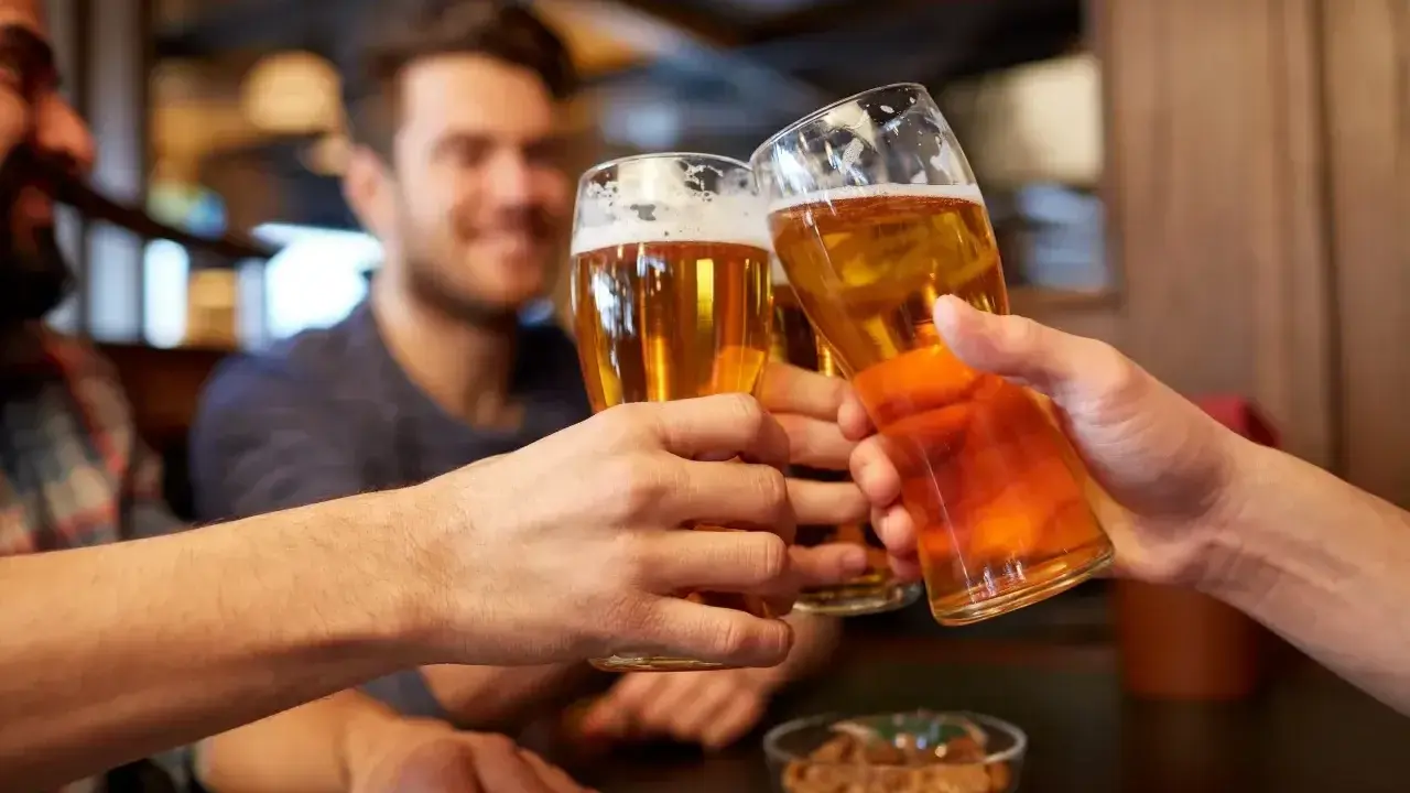 Trzech przyjaciół wznosi toast piwem. Widać ich dłonie trzymające szklanki z bursztynowym napojem, a na stole miseczkę z orzeszkami. To idealny moment, by porozmawiać o zawartości alkoholu w piwie.