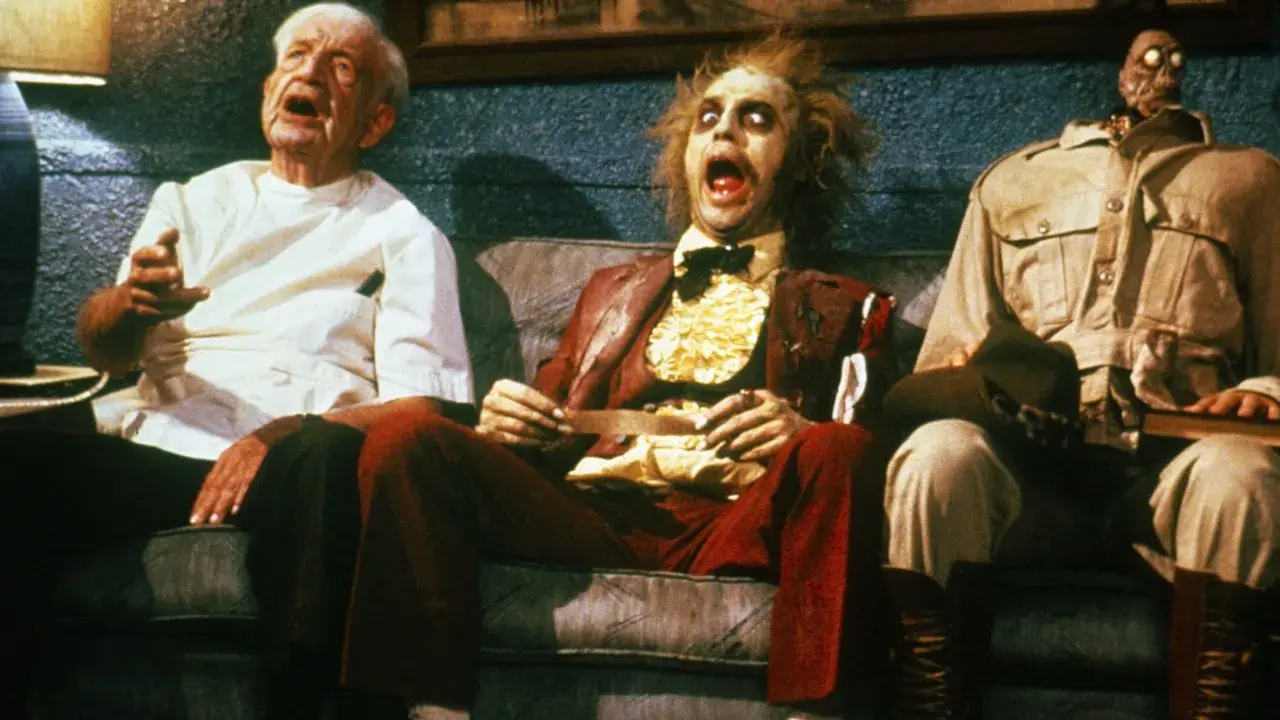 Tre personaggi bizzarri, tra cui Beetlejuice, siedono su un divano in una scena di horror comedy.