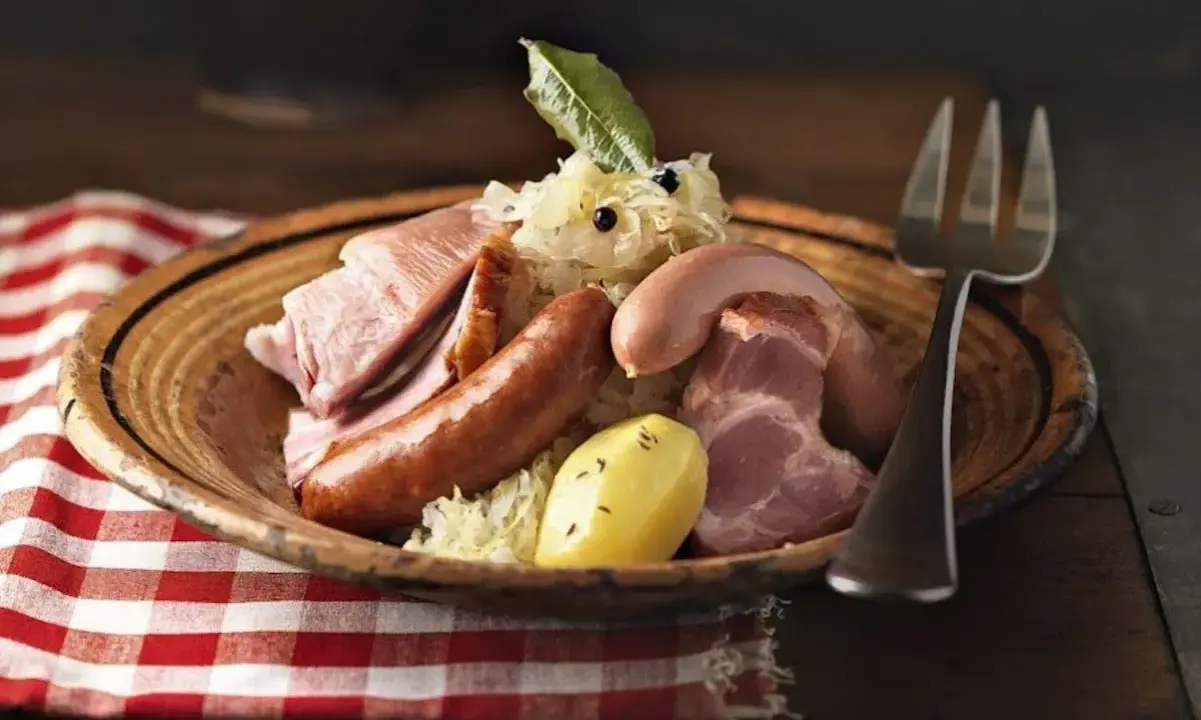 Assiette de choucroute garnie, évoquant son origine alsacienne, avec saucisses, lard, jambon et pommes de terre.