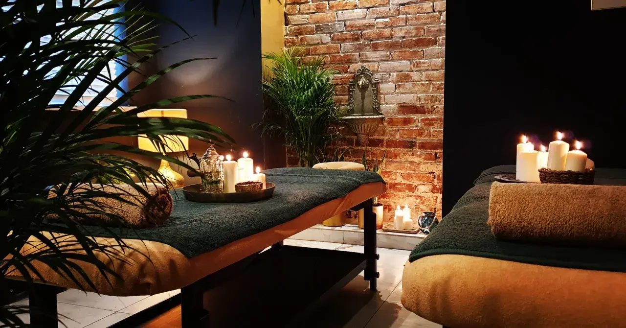 Dwie łóżka do masażu w przytulnym spa, ozdobione świecami i roślinami.