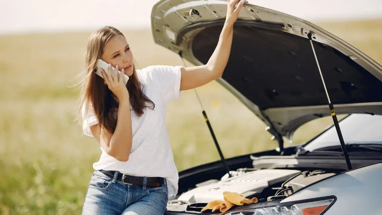 Mujer llama por teléfono con el capó abierto, preocupada por qué pasa si el coche se queda sin aceite.