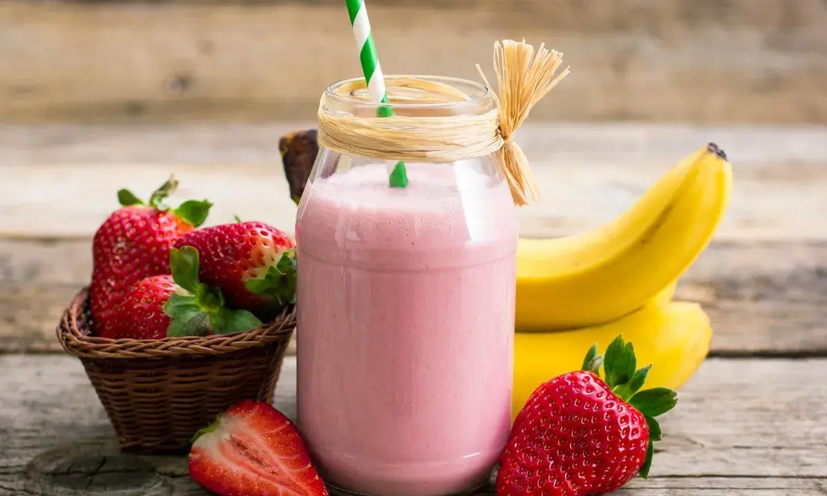 Delicioso batido de fresa y plátano, con fresas frescas y plátanos amarillos de fondo.