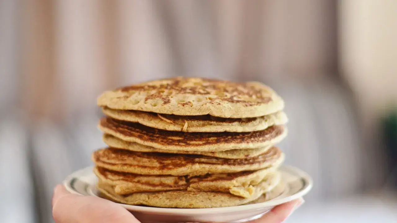 Pile de pancakes dorés à la farine de sarrasin, servis sur une assiette blanche tenue par une main.