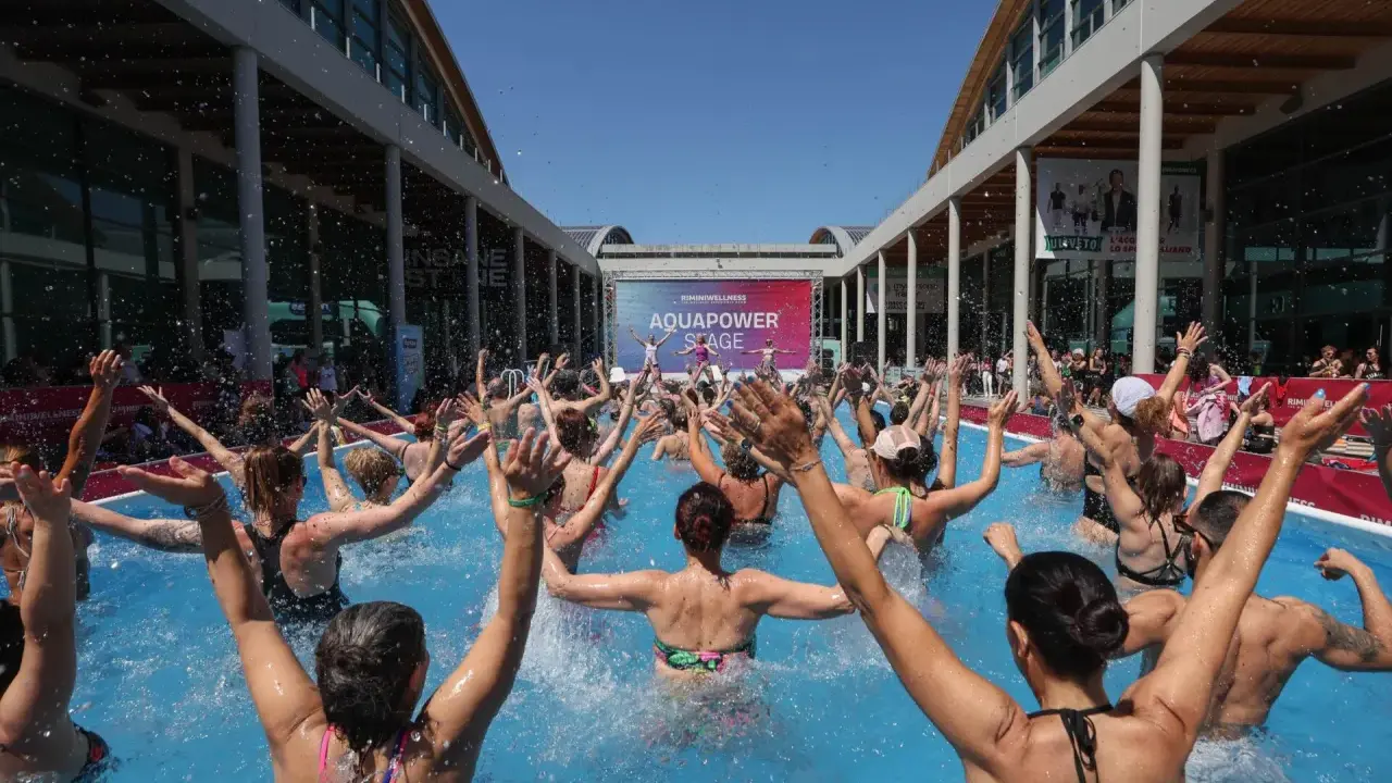 Folla entusiasta partecipa a una lezione di acquagym all'aperto, con le braccia alzate, durante la fiera dello sport Rimini.