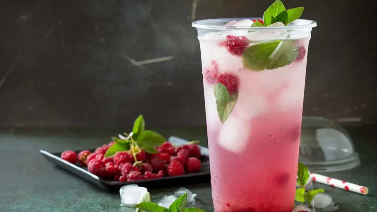 En uppfriskande raspberry daiquiri med färska hallon och mynta, serverad i ett plastglas med is.