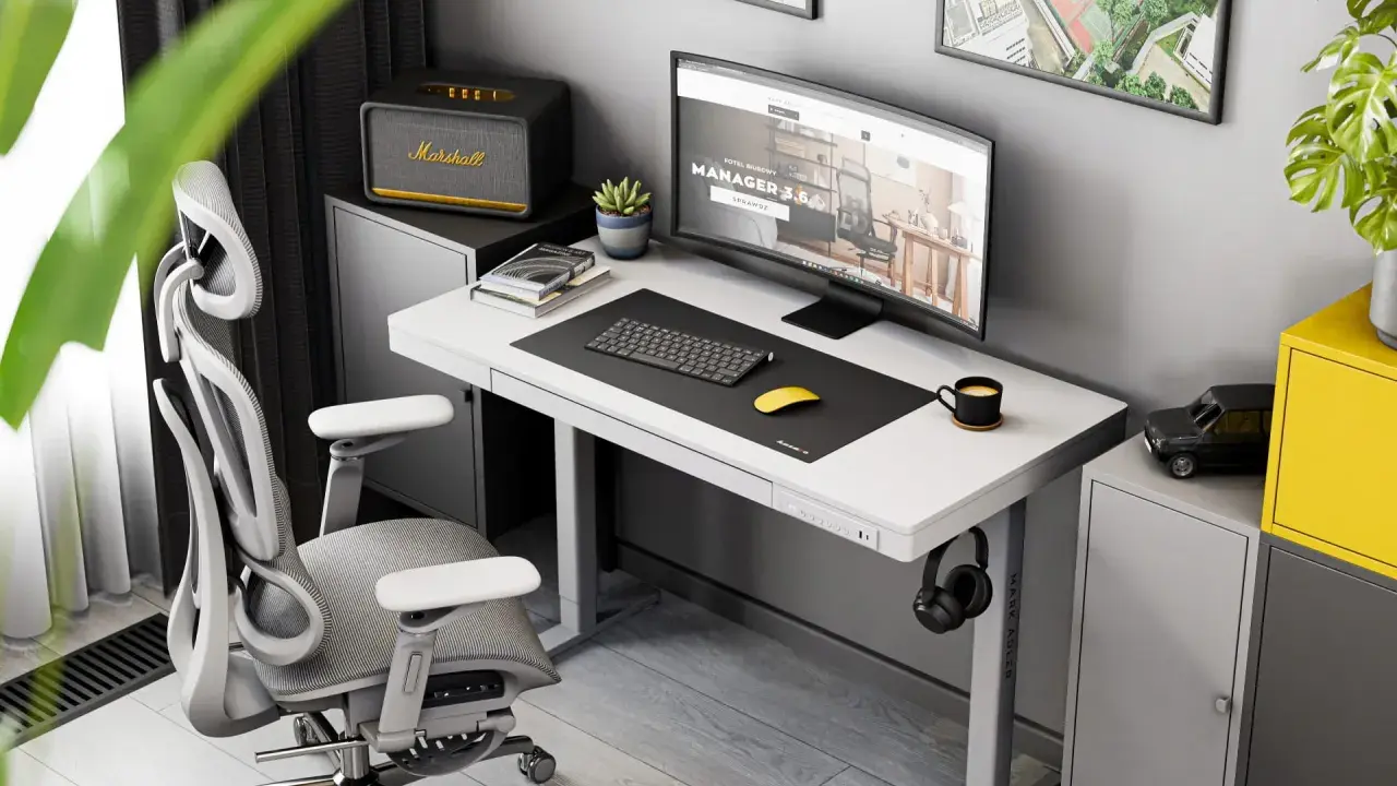 Ergonomiczne biurko do pracy przy komputerze z monitorem, klawiaturą i myszką. Obok stoi wygodny fotel biurowy i szafka z głośnikiem Marshall.