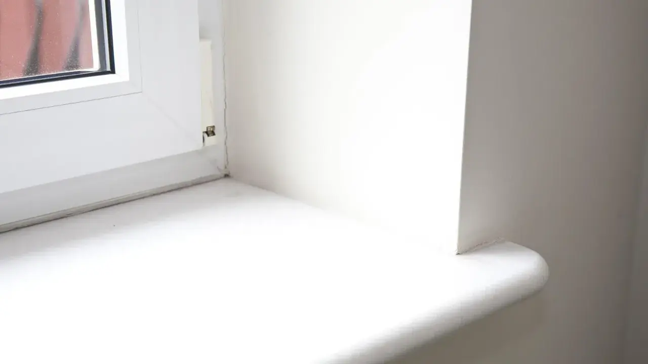 Biały parapet okienny, gotowy do wymiany. Widoczny fragment okna i ściany.