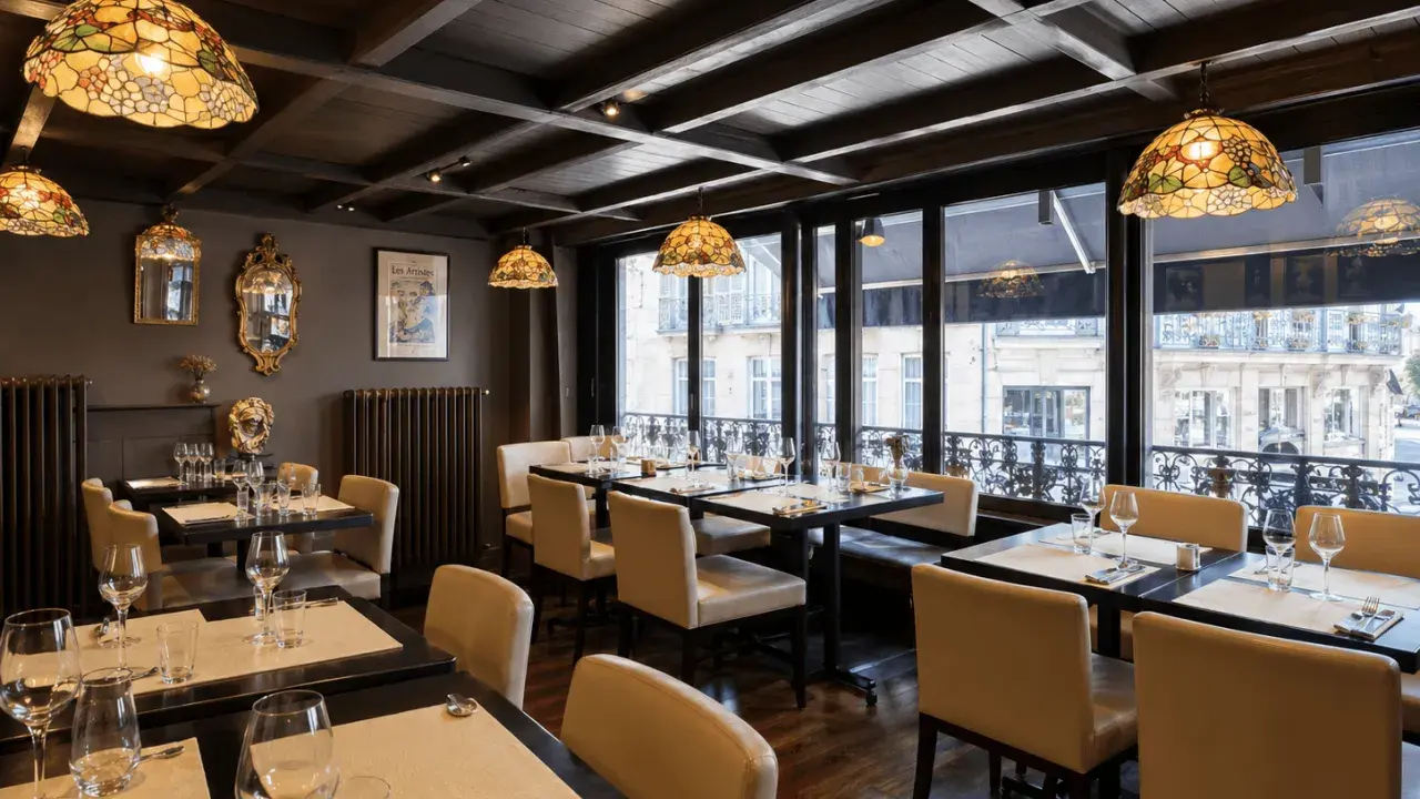 Salle à manger élégante avec des tables dressées, des luminaires Tiffany et une affiche "Les Artistes Limoges Menu" au mur.