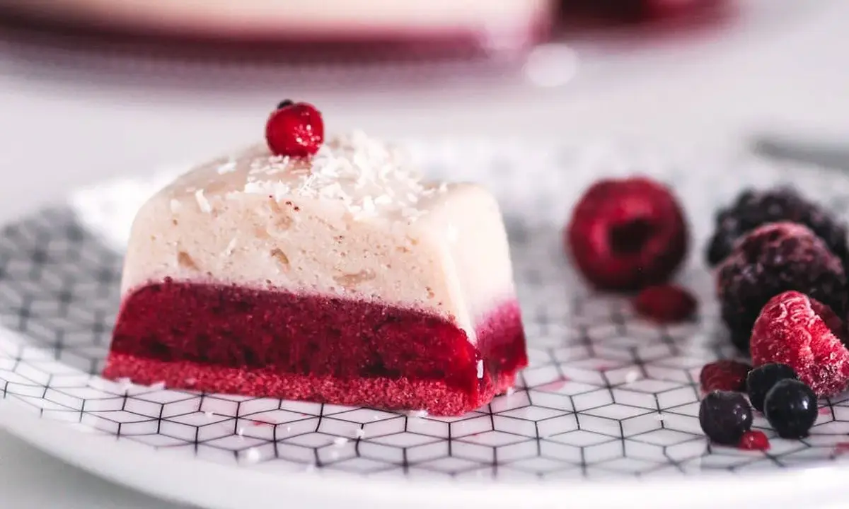 Deliciosa gelatina con agar agar, con capa roja de frutos rojos y capa superior cremosa, decorada con coco rallado y una baya.