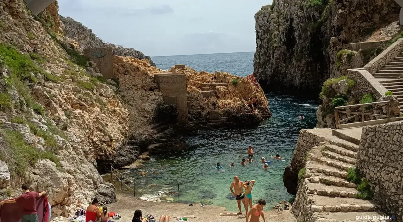 Santa Maria di Leuca: cosa vedere? Una caletta rocciosa con gente che nuota e si rilassa, con scalinate di pietra che scendono verso il mare cristallino.