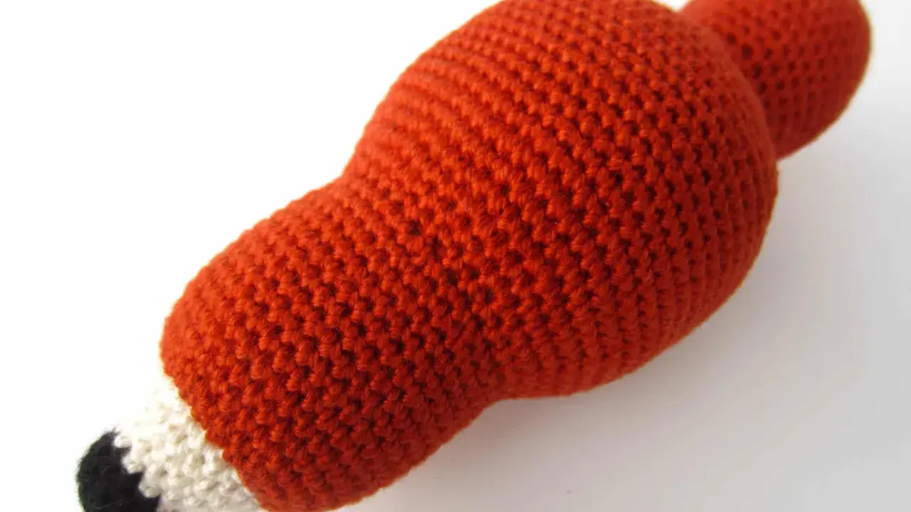 Un adorable zorro amigurumi de lana naranja, con detalles blancos y negros en el hocico, listo para jugar.