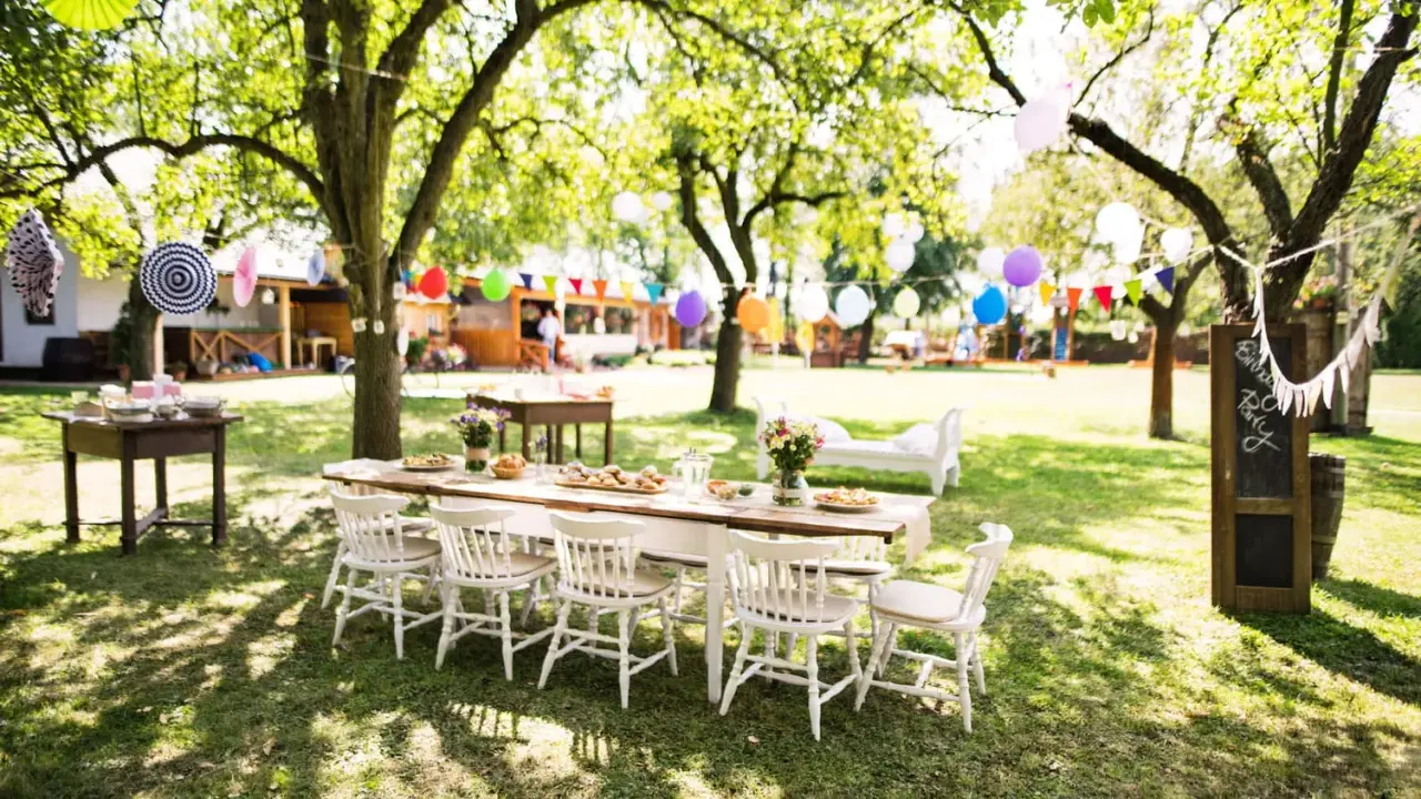 Une table dressée pour un repas en plein air, avec des guirlandes et des ballons, évoque une ambiance de deco jardin boheme chic.