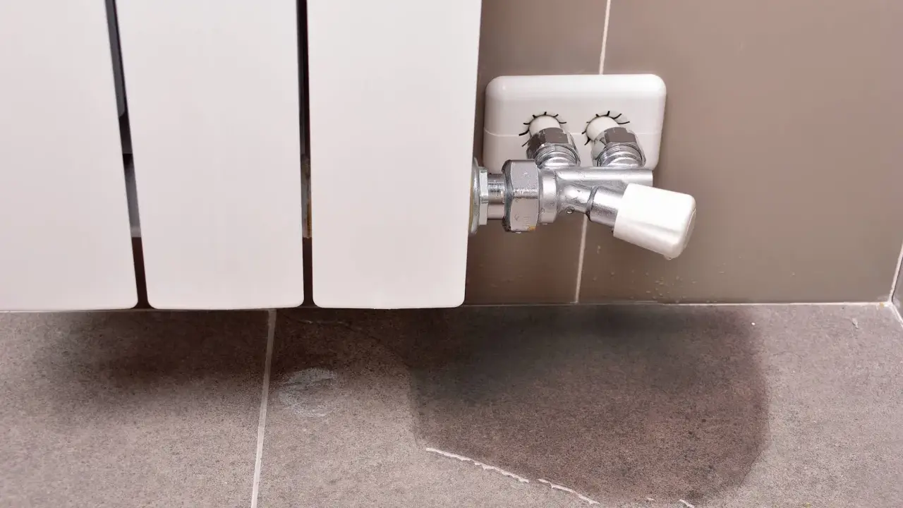 Un radiador que gotea deja un charco de agua en el suelo de baldosas, señal de un problema de fontanería.