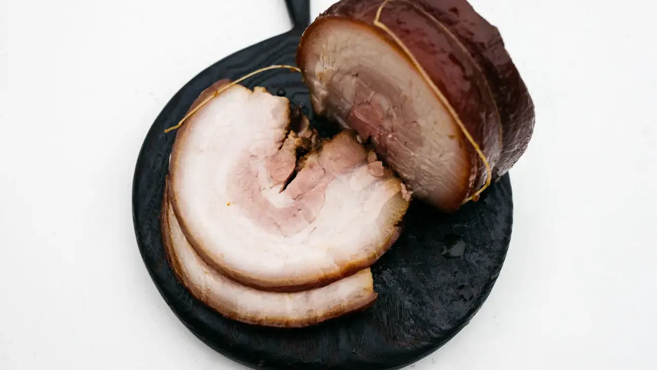 Pokrojony boczek chashu, z widocznymi warstwami mięsa i tłuszczu, ułożony na ciemnej desce.