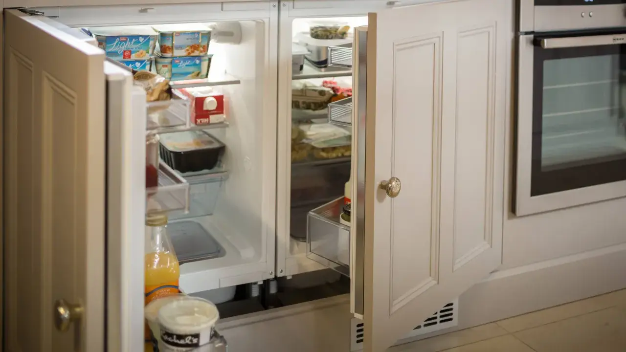 Un frigorifero integrato, quasi invisibile, con ante in legno che si fondono con l'arredamento, perfetto per nascondere il frigorifero in soggiorno.