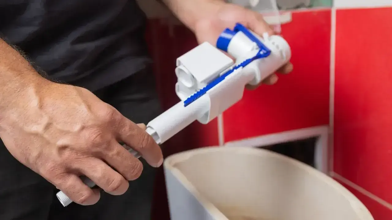 Ręce trzymają mechanizm spłuczki, przygotowując go do odkamieniania.