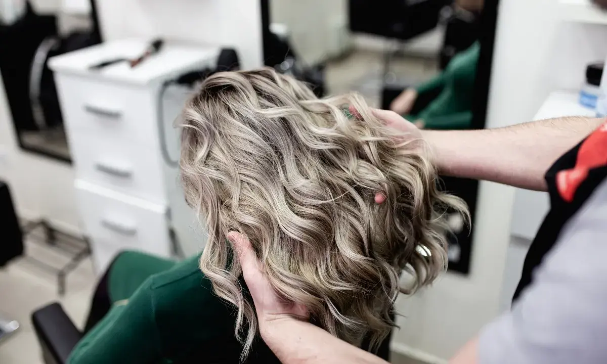 Profesjonalne usługi fryzjerskie: stylista układa falowane, blond włosy klientki w salonie.