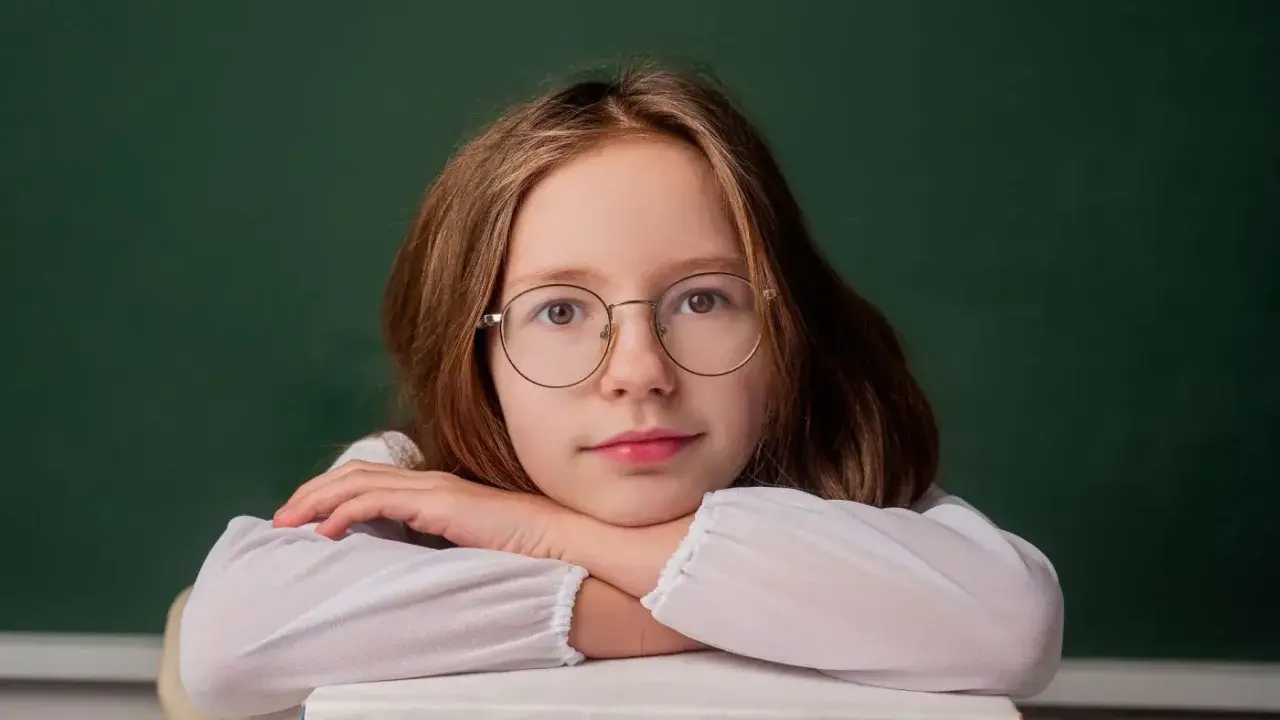 Dziewczynka w okularach opiera głowę na stosie książek. Zastanawia się, do kiedy można pobierać zasiłek rodzinny.