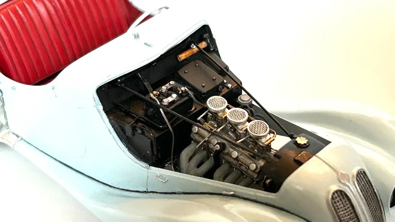 Detailansicht eines Modellautos mit rotem Lederinterieur und detailliertem Motor, dessen Teile mit Chromfolie veredelt sind.