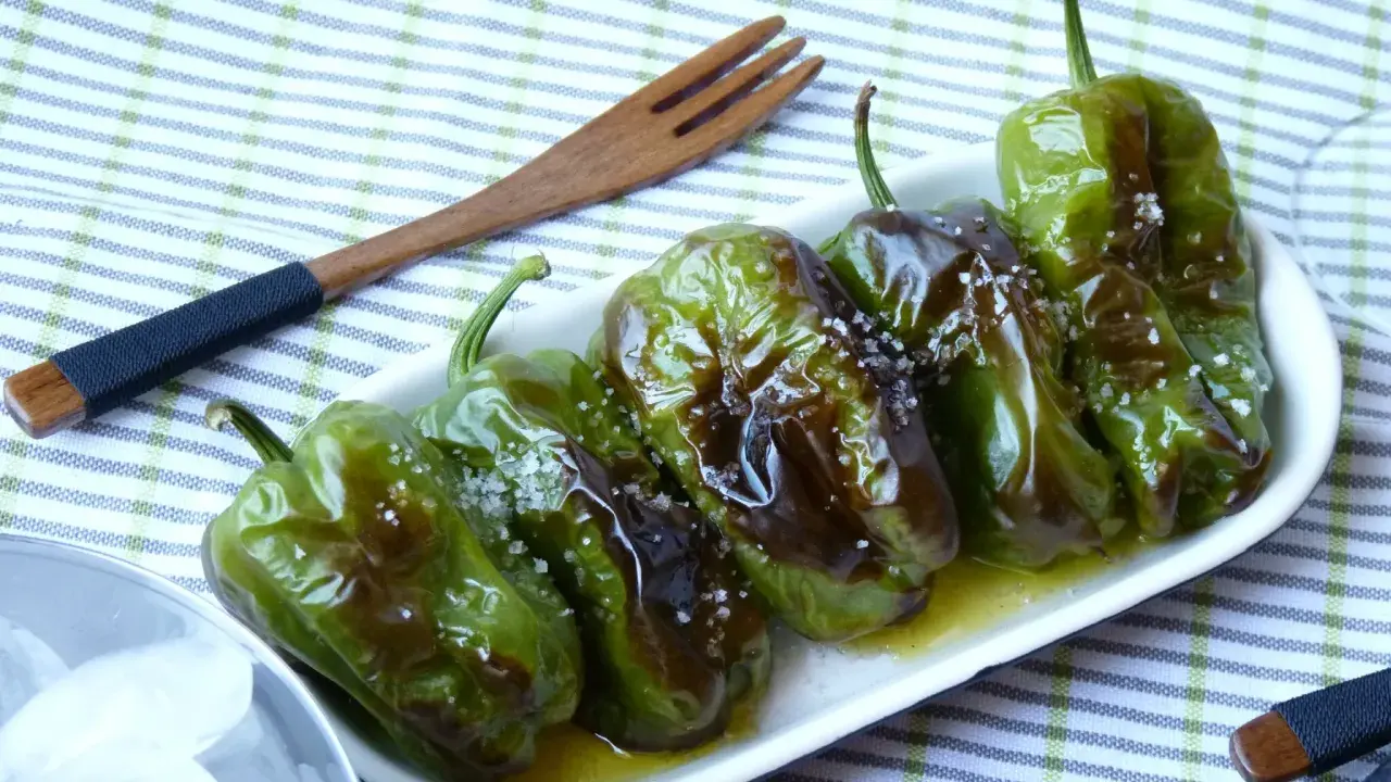 Délicieux **pieds de poivrons** verts, grillés et saupoudrés de gros sel, servis dans une assiette blanche avec une fourchette en bois.