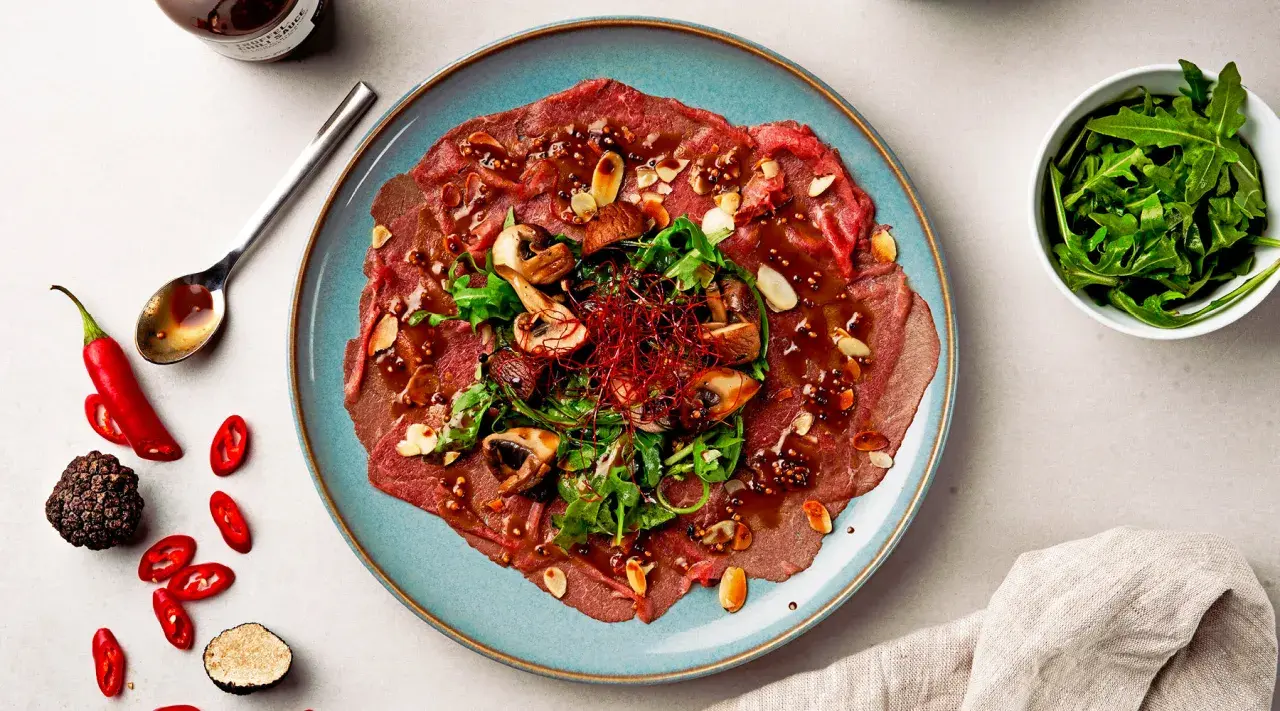 Rindercarpaccio mit Pilzen, Rucola und Mandeln. Eine köstliche Variation von Carpaccio, garniert mit Chili und Trüffel.